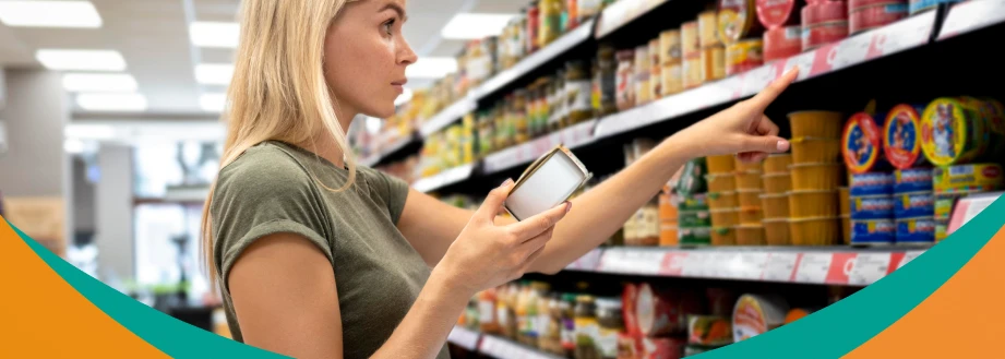 Uma mulher olhando para as prateleiras de um supermercado enquanto segura um celular, selecionando produtos.