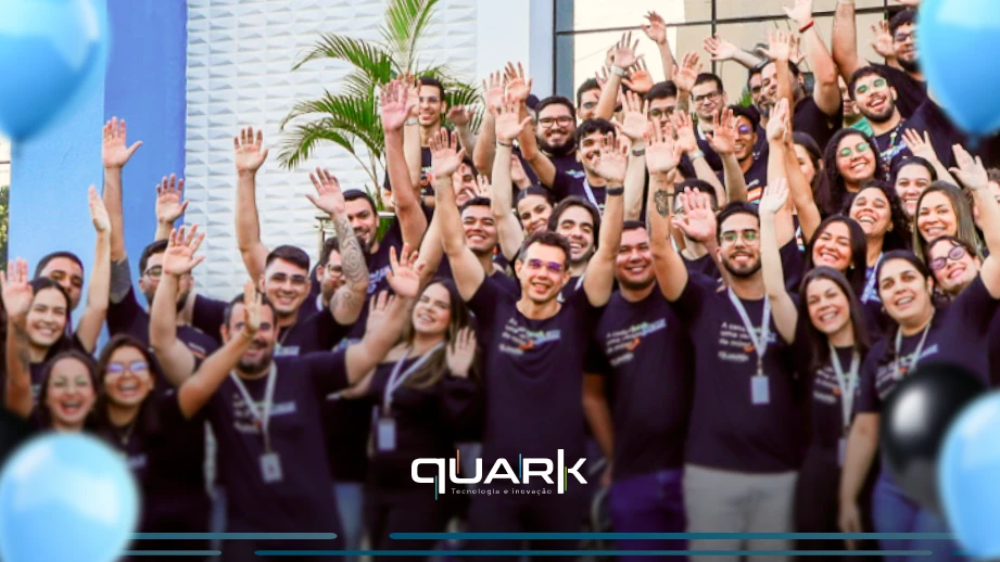 Grupo de colaboradores da Quark Tecnologia em evento de comemoração, sorrindo e celebrando juntos com balões azuis, simbolizando união e sucesso.
