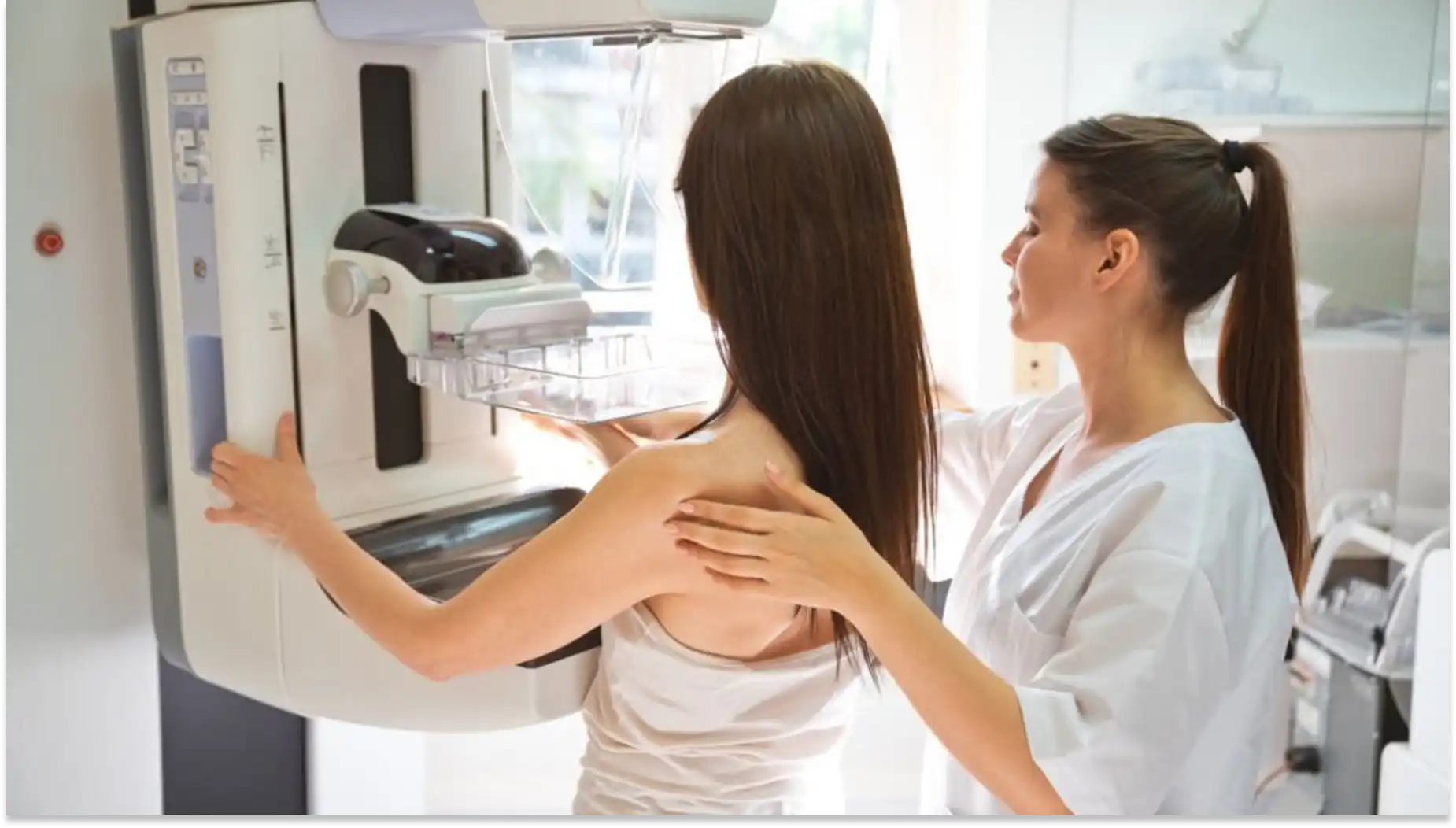 Mulher realizando mamografia em clínica de saúde, com acompanhamento de profissional de saúde ao lado. Exame de mamografia para detecção precoce do câncer de mama.