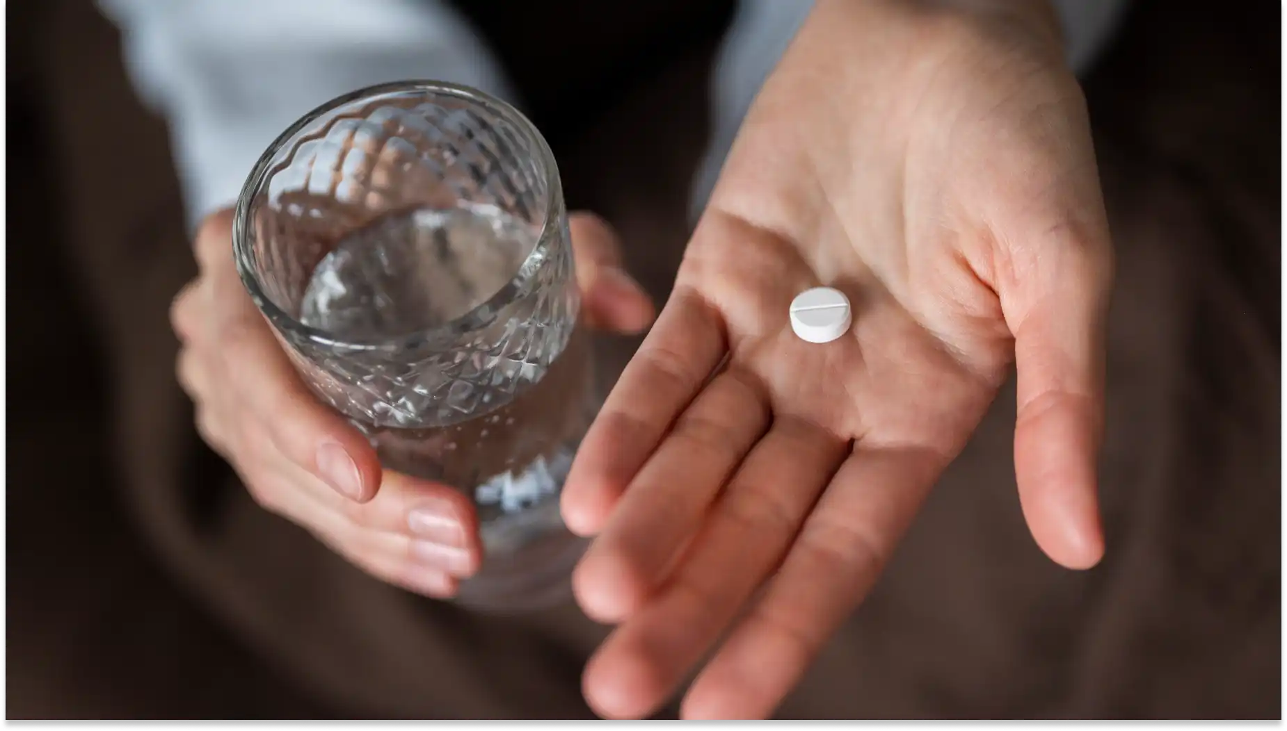 Imagem de uma pessoa segurando uma dose de paracetamol e um copo de água para consumo, relacionado a tratamentos para febre e dor.