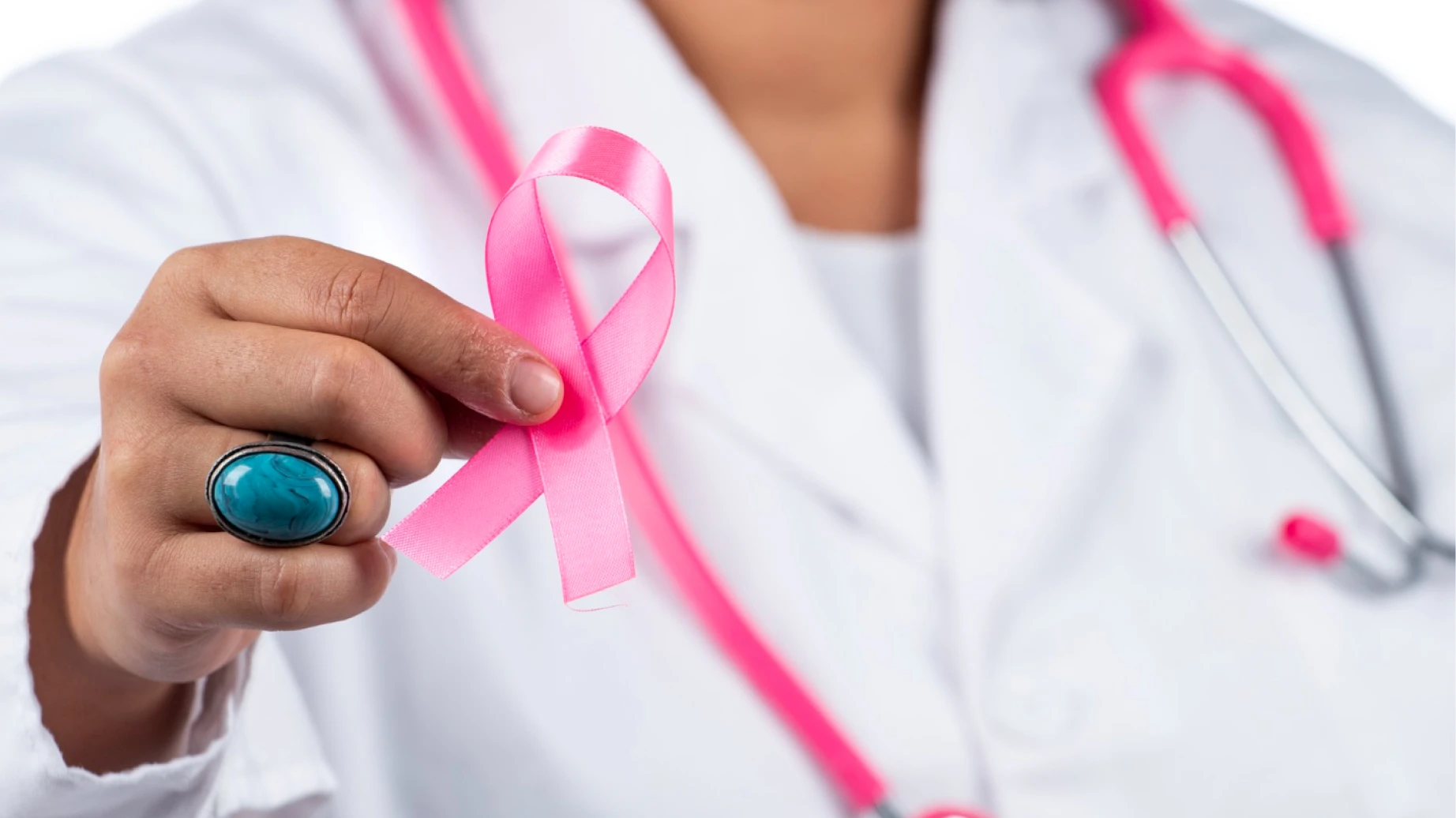Profissional de saúde segurando um laço de conscientização contra o câncer de mama, simbolizando apoio e prevenção, com estetoscópio rosa ao fundo.