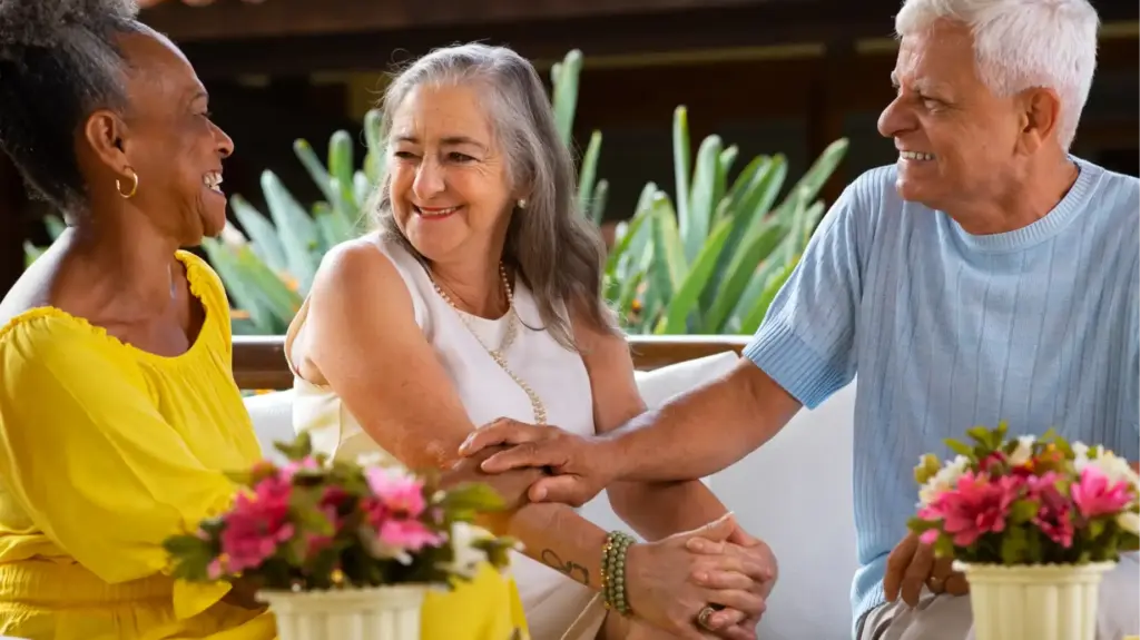 Três idosos sorridentes e felizes, conversando e se abraçando, enquanto desfrutam de um momento de convivência ao ar livre, refletindo otimismo com o envelhecimento, de acordo com pesquisa brasileira.
