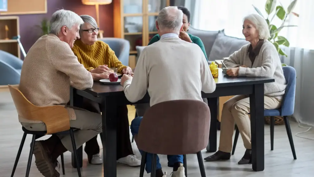 Grupo de idosos sorrindo e conversando ao redor de uma mesa, ilustrando os benefícios das amizades profundas para retardar o envelhecimento e proteger o cérebro.