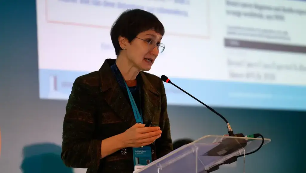 Profissional de saúde ou especialista falando em conferência sobre o aumento previsto de 77% nos casos de câncer até 2050, conforme projeções da OMS.