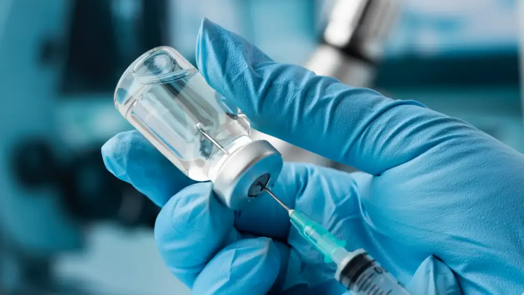 Imagem de uma pessoa com luvas médicas segurando uma ampola de vacina e uma seringa, simbolizando avanços no combate à SRAG no Brasil, com queda nos casos segundo a Fiocruz.