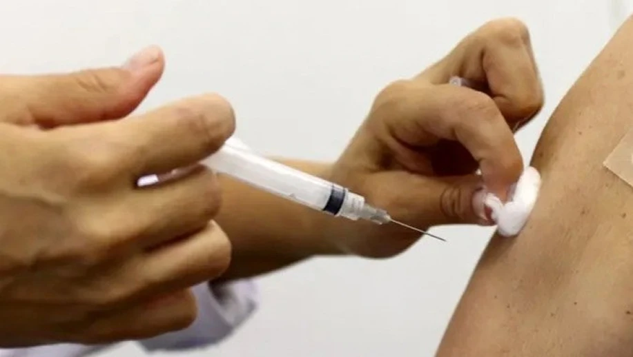 Aplicação de vacina contra pneumonia com seringa em um braço, mostrando as mãos do profissional preparando a injeção para administração intramuscular.